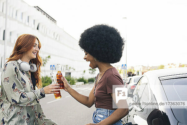 Fröhliche Afro-Frau stößt mit einer Freundin am Straßenrand auf Bierflaschen an
