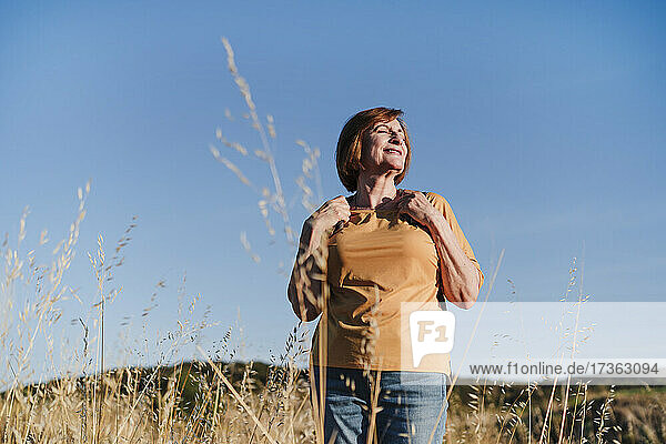 Lächelnde ältere Frau mit geschlossenen Augen beim Wandern an einem sonnigen Tag