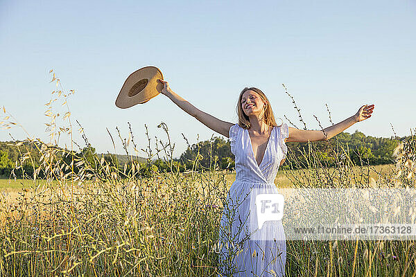 Fröhliche junge Frau mit Hut inmitten von Gras auf einem Feld