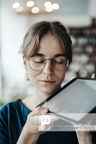Freiberuflerin mit geschlossenen Augen  die ein digitales Tablet in einem Café hält