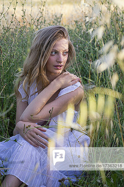 Beautiful woman looking away while sitting amidst grass in field