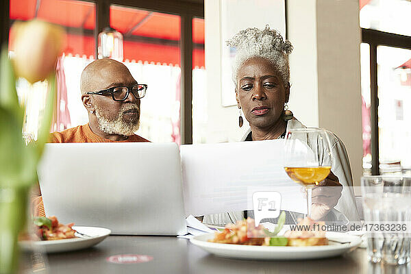 Ältere Frau prüft Papier  während sie mit einem Mann im Restaurant diskutiert