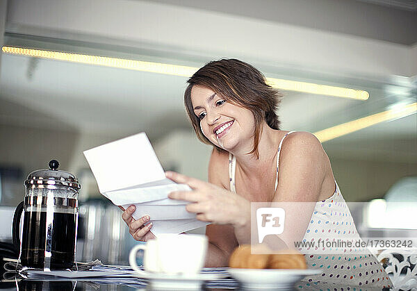 Lächelnde junge Frau  die an der Kücheninsel sitzend einen Brief liest