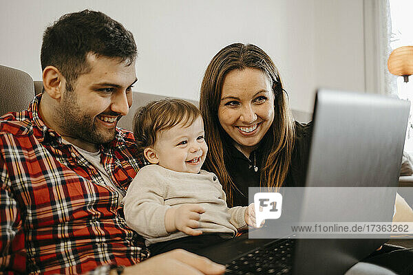 Baby-Junge mit Eltern lächelnd im Gespräch während Video-Anruf durch Laptop zu Hause