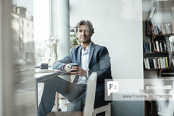 Geschäftsmann hält Kaffeetasse  während er in einem Cafe sitzt