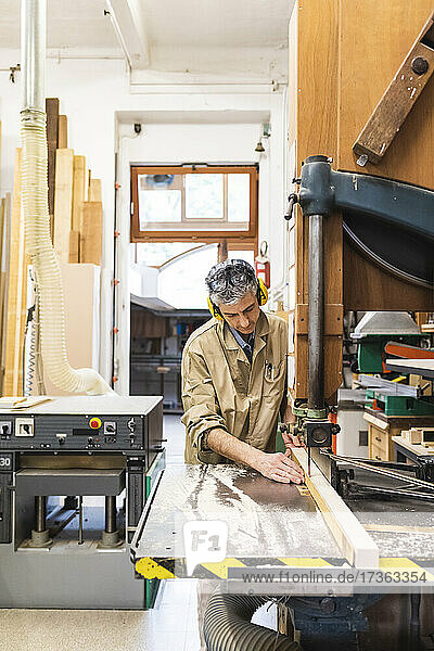 Mature male carpenter using machine while working at workshop