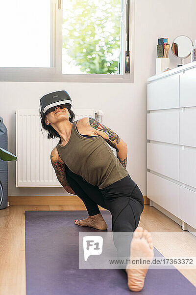 Woman doing stretching exercise while wearing virtual headset at home