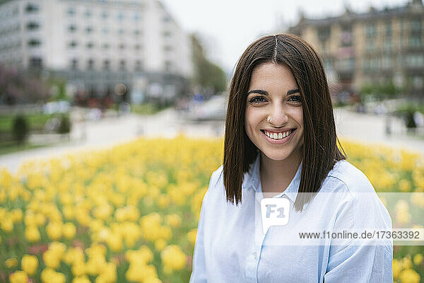 Lächelnde schöne junge Frau vor gelb blühenden Pflanzen