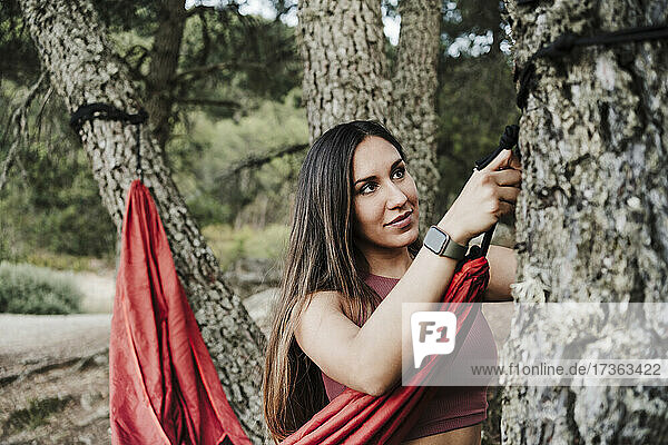 Frau bindet Seil der Hängematte an Baum im Wald