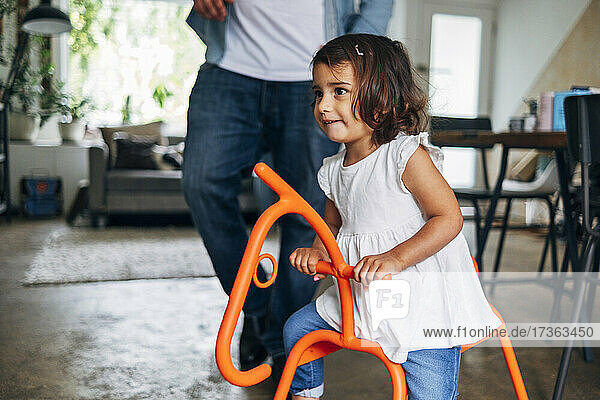 Cute girl playing on rocking horse while father in background at home