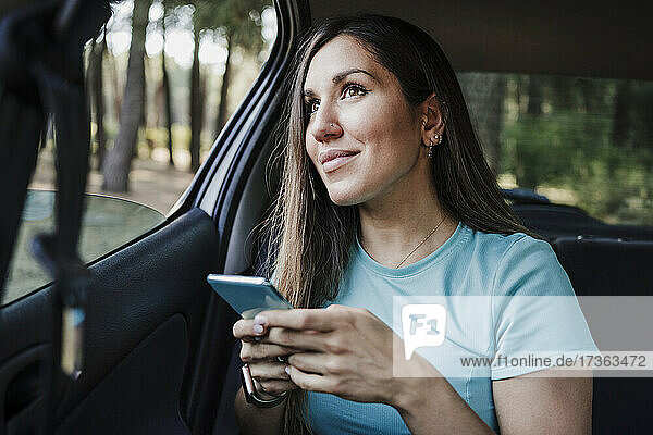 Junge Frau mit Handy in der Hand im Auto sitzend