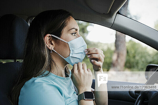 Junge Frau mit Gesichtsschutzmaske im Auto während COVID-19
