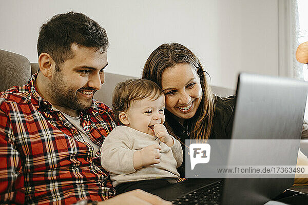 Glückliche Mutter und Vater mit Sohn während eines Videogesprächs auf dem Laptop im Wohnzimmer sitzend