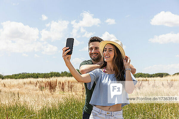 Lächelnde Frau nimmt Selfie mit Freund durch Smartphone auf sonnigen Tag