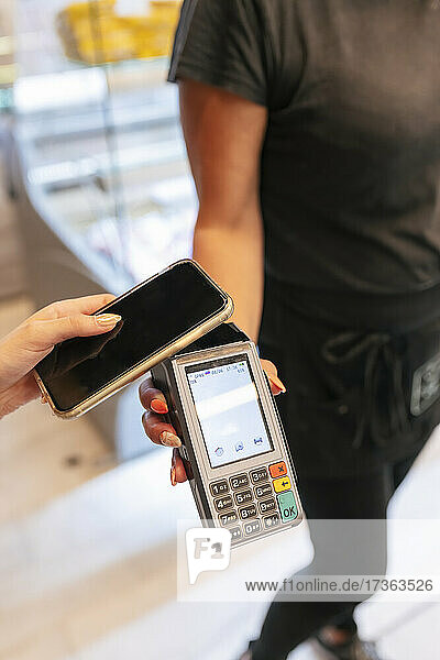 Frau  die mit ihrem Mobiltelefon online bei einer Kellnerin im Restaurant bezahlt