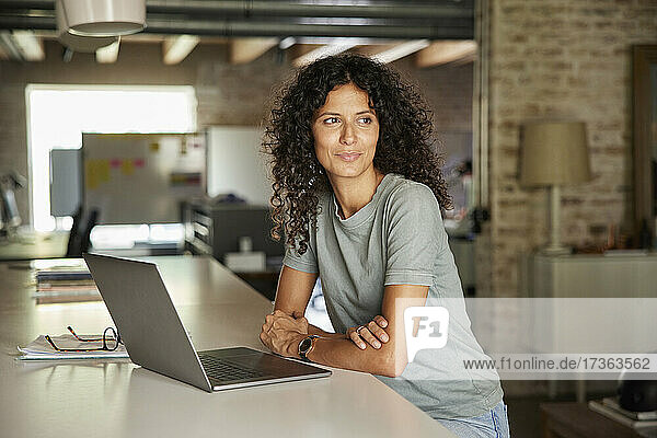Thoughtful businesswoman looking away while sitting with laptop at workplace
