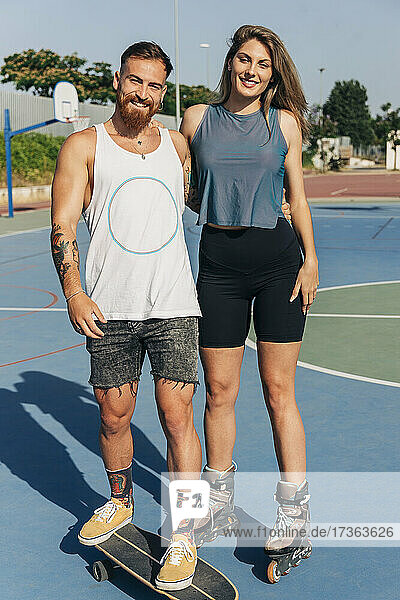 Lächelndes junges Paar  das sich auf dem Basketballplatz an einem sonnigen Tag in den Armen liegt