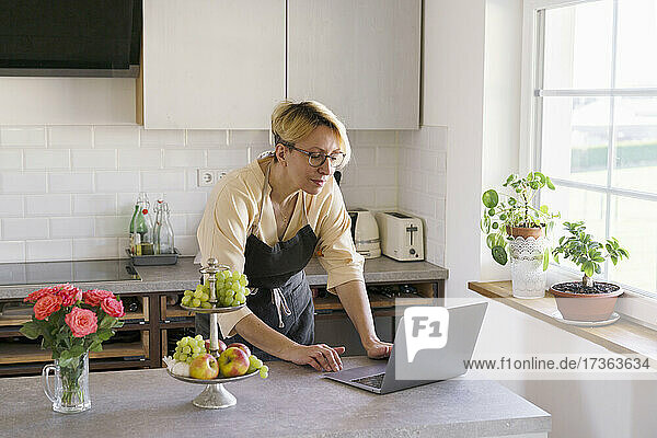 Berufstätige Frau in Schürze mit Laptop in der Küche