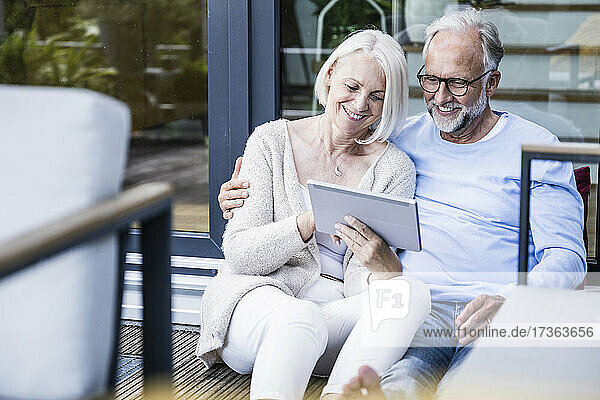 Lächelnde Frau  die ein digitales Tablet benutzt und neben einem Mann auf dem Balkon sitzt