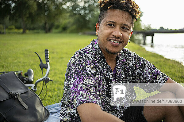 Lächelnder Mann mit Rucksack und Fahrrad auf einer Wiese sitzend