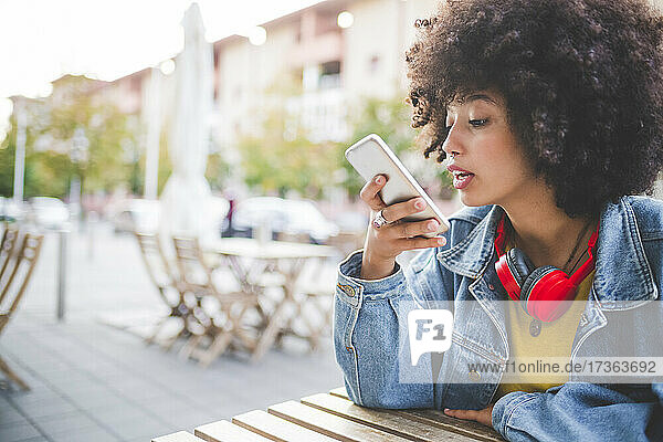 Junge Frau mit Afrofrisur benutzt ihr Smartphone in einem Café im Freien in der Stadt