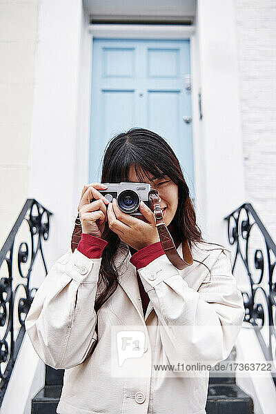 Junge Frau fotografiert mit analoger Kamera vor einem Gebäude