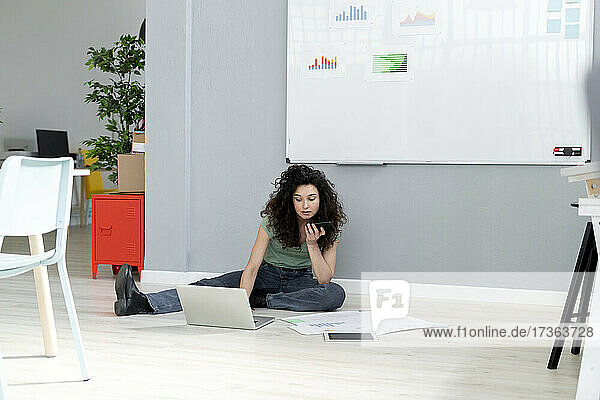 Businesswoman talking on mobile phone while working through laptop at office