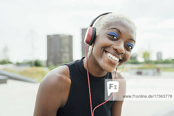 Glückliche Frau hört Musik über Kopfhörer im Park