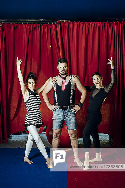 Weibliche Akrobaten mit erhobener Hand stehen mit einem männlichen Darsteller im Zirkus