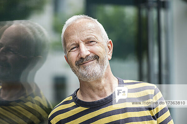 Älterer Mann  der sich lächelnd an eine Glaswand lehnt