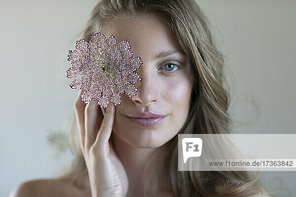 Blonde junge Frau bedeckt ihr Auge mit einer Wildblume im Studio