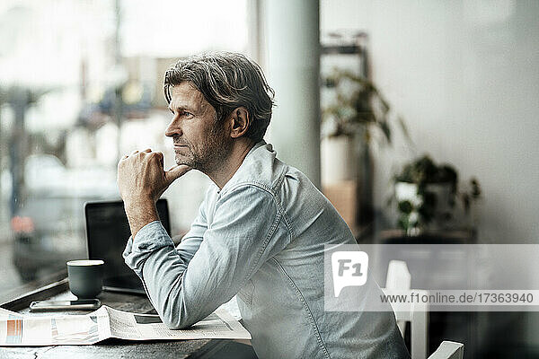 Nachdenklicher Mann sitzt mit Zeitung und schaut durch das Fenster  während er in einem Café sitzt