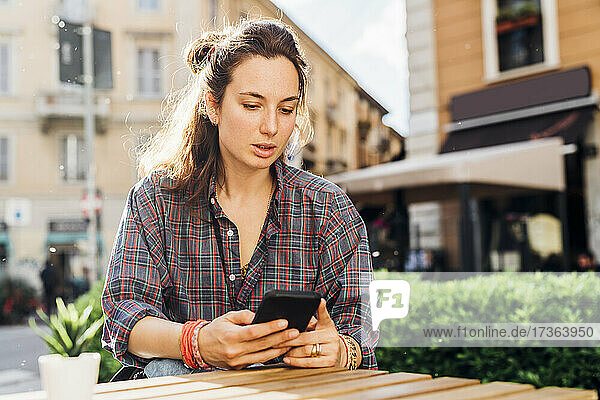Frau benutzt Smartphone  während sie an einem sonnigen Tag in einem Straßencafé sitzt