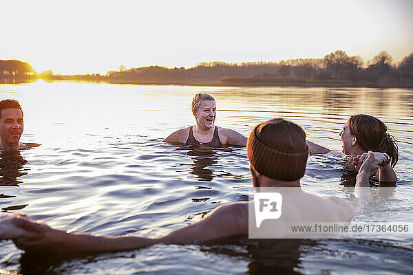 Frauen mit männlichen Freunden lachen  während sie sich im kalten Wasser am Morgen vergnügen