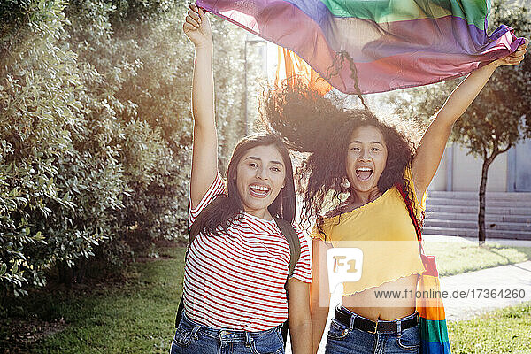 Sorglose lesbische Frauen winken bei Sonnenuntergang mit der Regenbogenflagge