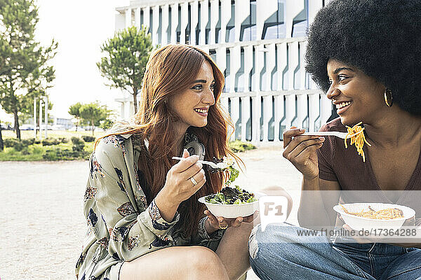 Smiling young women having food while talking during sunny day