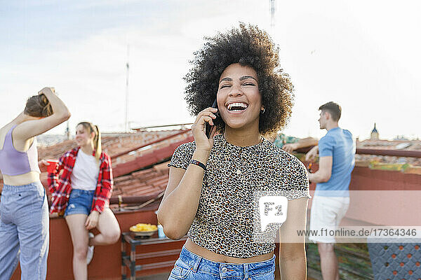 Junge Frau lacht  während sie in einer Party auf der Terrasse mit ihrem Smartphone telefoniert