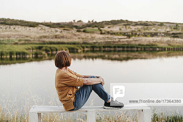 Ältere Frau mit Blick auf die Berge  während sie auf einer Bank in der Nähe eines Sees sitzt
