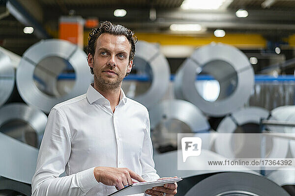 Thoughtful businessman holding digital tablet in factory