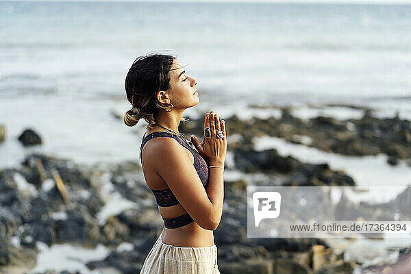 Junge Frau mit verschränkten Händen übt Yoga am Strand