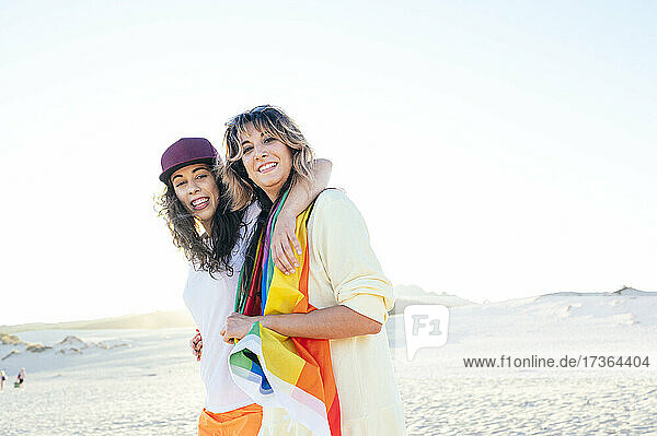 Happy young woman with arm around girlfriend at beach
