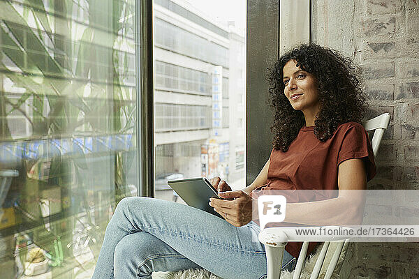 Geschäftsfrau hält digitales Tablet und sitzt am Fenster