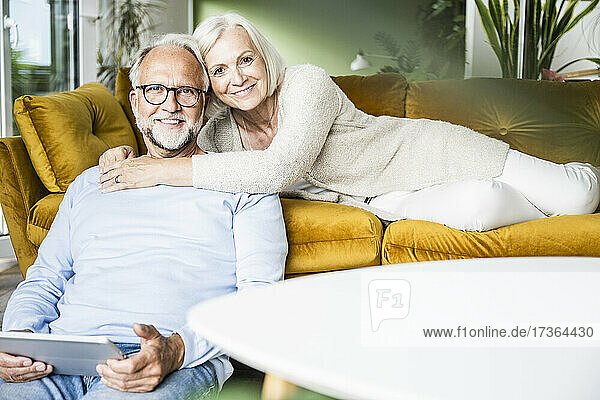 Lächelnde Frau  die einen Mann umarmt  während sie sich zu Hause auf dem Sofa ausruht