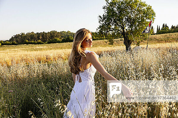 Schöne Frau im weißen Kleid berührt Pflanzen auf einem Feld
