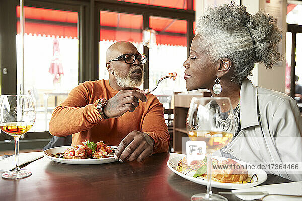 Reifer Mann füttert Frau im Restaurant sitzend
