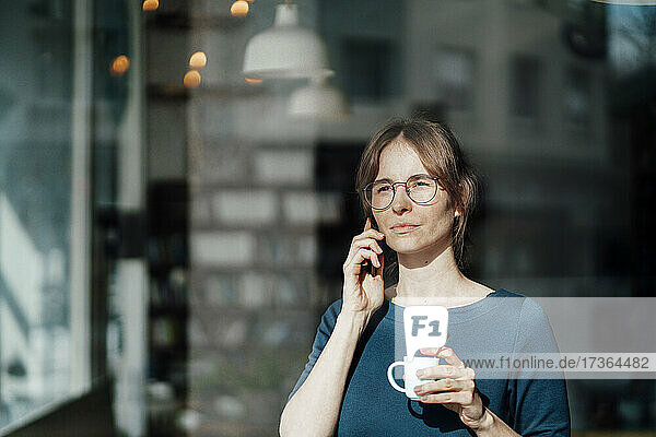 Junge Frau hält Kaffeetasse und spricht mit Smartphone