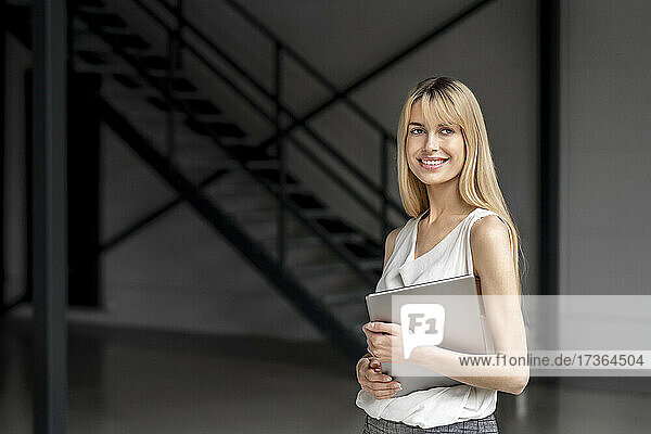Smiling young female professional holding laptop at office