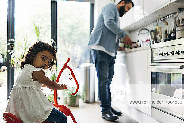 Girl sitting on rocking horse toy while father at kitchen counter
