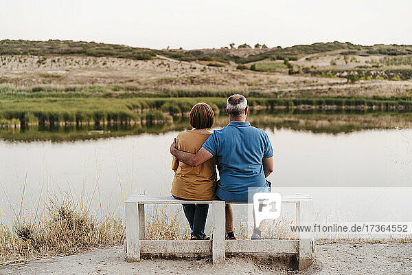 Son with arm around mother sitting on bench near lake