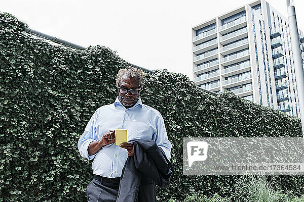 Geschäftsmann  der ein Mobiltelefon benutzt  während er vor einer grünen Wand steht